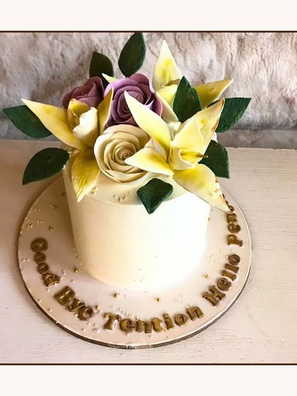 A simple and elegant cake topped with a bouquet of yellow and purple sugar lilies and roses, with the message "Good Bye Tention Hello Pension".
