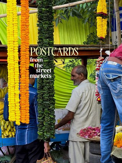 'Postcards from the street markets', featuring a vendor selling long garlands of marigolds.
