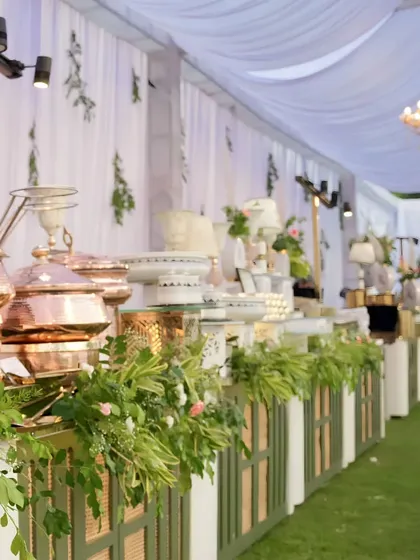An expansive view of an elegant buffet setup for an outdoor corporate luncheon. Our signature hammered copper serveware and fresh floral arrangements create a visually stunning centerpiece for any gathering.