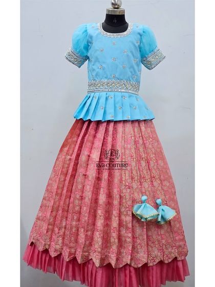 A lovely combination of sky blue and pink. This lehenga features a pleated peplum blouse and a layered skirt with a scalloped hem.