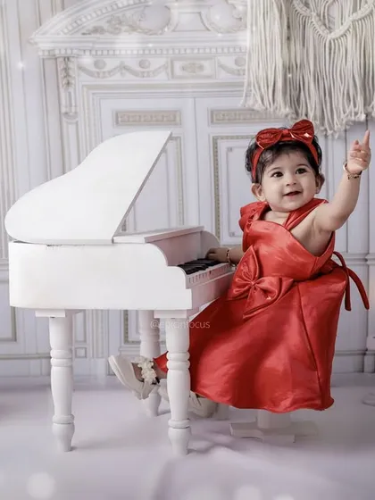 Dressed in a stunning red gown, this little musician is ready for her piano recital. The elegant all-white set creates a sophisticated and timeless portrait.
