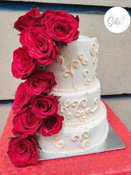 A dramatic and romantic three-tier cake featuring a cascade of deep red roses against a backdrop of white buttercream with delicate piping. This design makes a bold and beautiful statement.