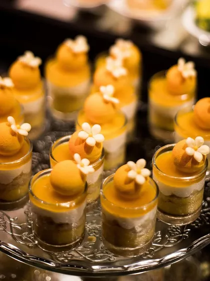 A tray of beautiful mango mousse desserts. The vibrant colour and delicate floral garnish make this a refreshing and elegant end to any meal.