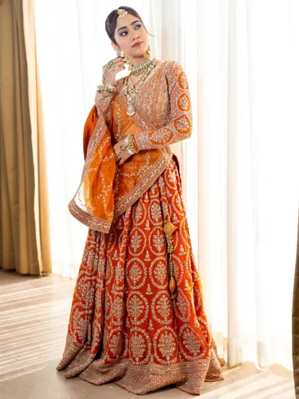 A full length shot of the vibrant orange lehenga, showing its grand flare and intricate detailing.