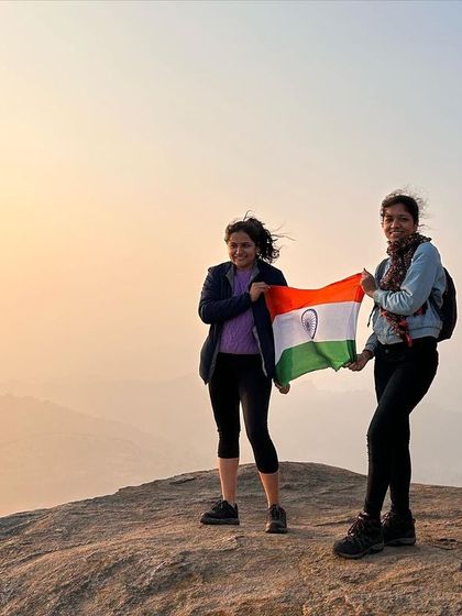 Two trekkers hold the Indian flag at the summit of Huthridurga, celebrating Republic Day with a patriotic sunrise.