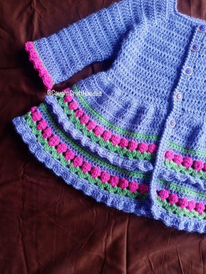 A detailed shot of the textured stitching on our light purple baby cardigan. You can see the care that goes into each bobble and ruffle, creating a truly special handmade garment.
