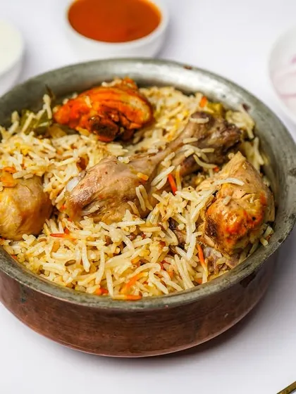 A handi of authentic chicken biryani, served with three different chutneys and pickled onions. The bright, even lighting ensures all components of the dish are clearly visible.