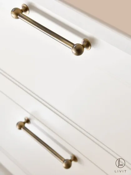 Our Sphere cabinet pulls in an antique brass finish, installed on the drawers of a kitchen island. The simple, clean design provides a touch of vintage elegance to the soft white cabinetry.