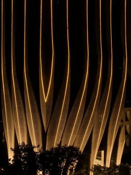 The illuminated facade at night, viewed from the base. The design creates a sense of movement and elegance, transforming the building into a piece of urban sculpture.