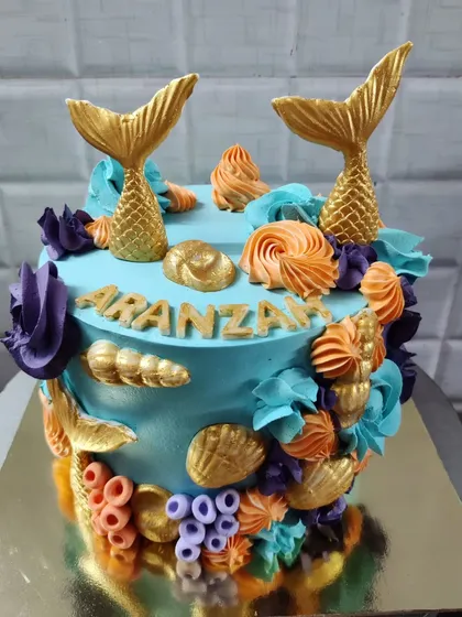 An enchanting mermaid-themed cake perfect for a magical birthday. This custom cake is decorated with golden mermaid tails, colorful buttercream corals, and delicate seashells.