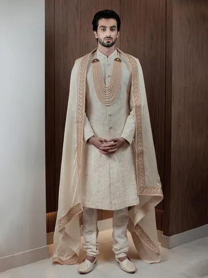 For the groom who desires nothing less than royalty. This ivory sherwani, complete with a regal cape and a multi-layered pearl necklace, is designed to make a grand statement on your most important day.