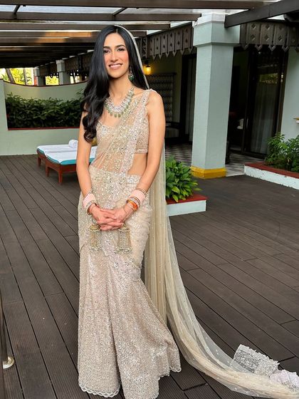 The full view of the minimalist bride. Her makeup is light and airy, a perfect match for the elegant, shimmering saree and the outdoor wedding setting.