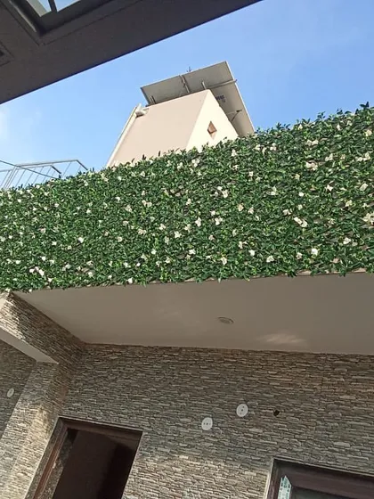 An artificial green hedge with white flowers installed on the top of a balcony wall. This adds privacy and a touch of garden charm to the home's exterior.