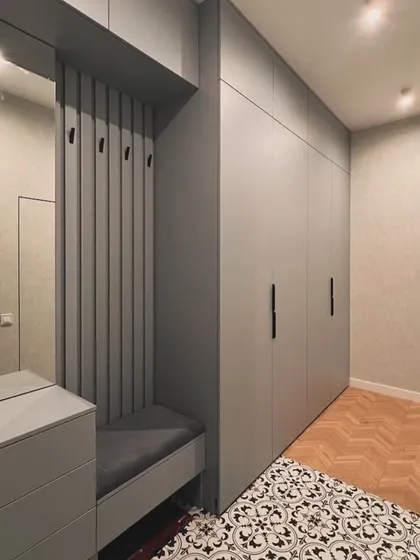 A wider shot of the wardrobe and entryway unit, showing how it fits perfectly into the room. The combination of herringbone wood flooring and patterned tiles defines the different functional zones.