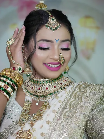 The joy of a bride on her special day. This close-up captures her happy expression and the vibrant pink eye makeup that complements her white and green bridal ensemble.