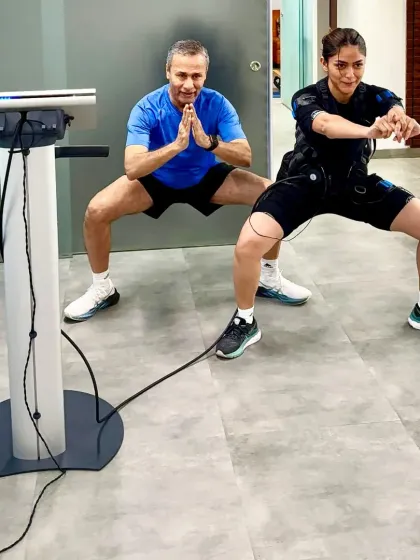 A sumo squat pose, which targets the inner thighs and glutes. The EMS suit ensures these muscles are working at their maximum potential.