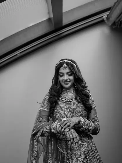 A beautiful black and white portrait of the bride, looking down with a gentle smile. This timeless style highlights her intricate jewelry and the serene emotion of the moment.