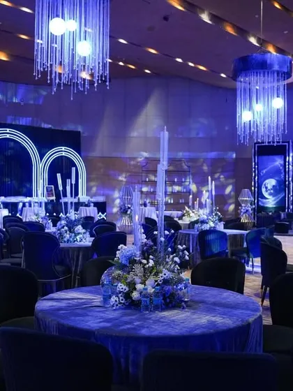 The entire event space bathed in a cool blue light, showing the cohesive design from the dining tables to the stage and lounge areas.