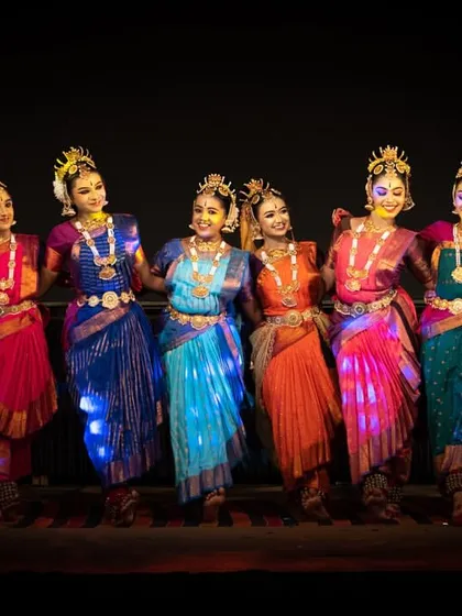 Our gopi dancers in a line, showcasing their vibrant, multi-colored costumes. The lighting on their dresses adds a magical, sparkling effect to their presence on stage.