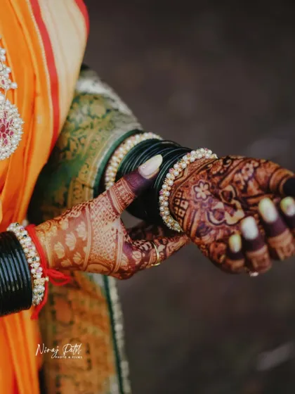 A beautiful shot of the bride's hands, showcasing the rich, dark mehendi stain against her traditional wedding attire and bangles.