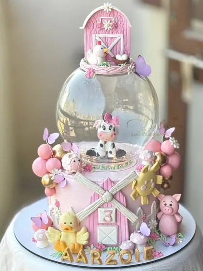 A pink farmland theme cake for a third birthday. This design features a globe tier and lots of cute, hand-modelled farm animals like a cow, pig, and chicken.