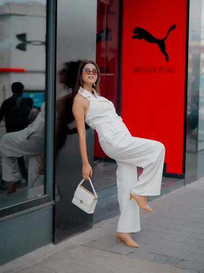 A full-length shot of a model in a chic white outfit, posing in front of a store. This captures a modern, commercial fashion look.