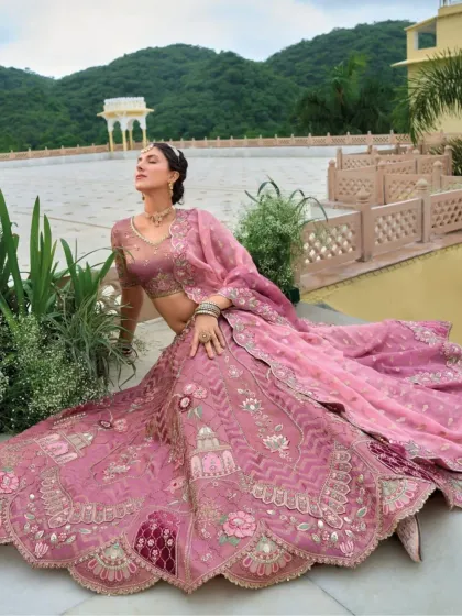A dramatic seated pose that showcases the full, flowing skirt of the dusty rose lehenga and its intricate, artistic embroidery.