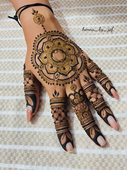 A striking mandala design centered on the back of the hand, featuring a large, detailed floral pattern. The fingers are adorned with complementary patterns and solid tips for a bold look.