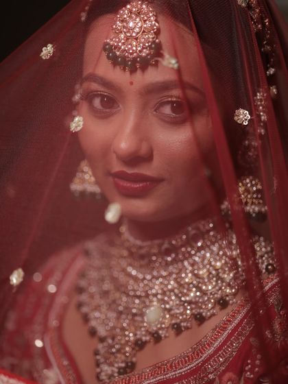 A captivating shot of my bride Krupa through her red veil. Her look features soft, sculpted skin, a flush of rose, and bold eyes for a timeless bridal glow.