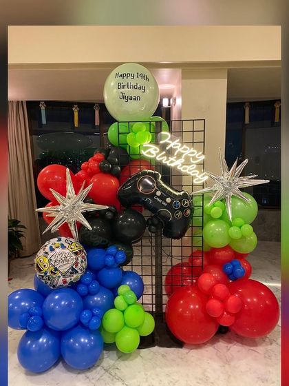 A full view of the awesome gaming-themed balloon installation. The vibrant red, blue, green, and black balloons pop against the metal grid, creating an exciting focal point for a teen's birthday party.