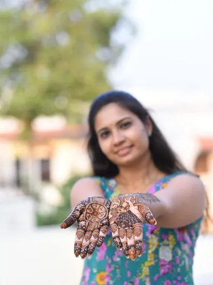 A happy client showing her traditional mehndi design. The focus is on the beautiful patterns on her palms, which include a chakra and peacock motifs.