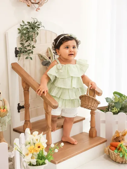 Exploring her world. This candid shot captures a toddler's curiosity as she stands by a rustic staircase prop. The soft, natural tones of the setup create a gentle and timeless look.