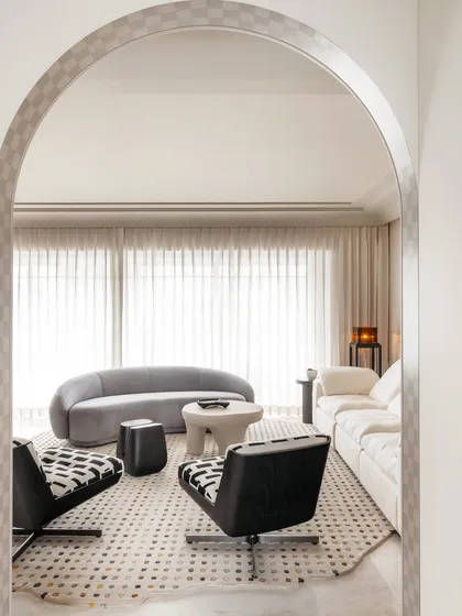 This view of Apartment O2 shows the interplay of different textures and forms, from the patterned swivel chairs to the smooth, curved sofa. The checkered archway adds a playful architectural detail.