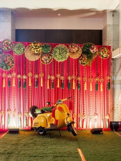 A fun and quirky photo booth with a bright yellow scooter. The backdrop of red drapes and hanging tassels provides a vibrant and playful spot for guests to take pictures.