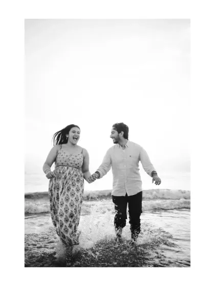 A dynamic shot of a couple running and splashing in the waves. The black and white format adds a classic, nostalgic feel to this moment of pure, energetic fun.