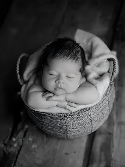 A simple basket pose in black and white creates a timeless and artistic feel. The focus remains entirely on the baby's serene expression and tiny, folded arms.