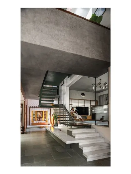 The interior is defined by interlocking volumes and honest materials. A heavy, form-finished concrete beam defines the edge of a double-height space, with floating marble steps leading down into the main living area, creating a dramatic sectional play.