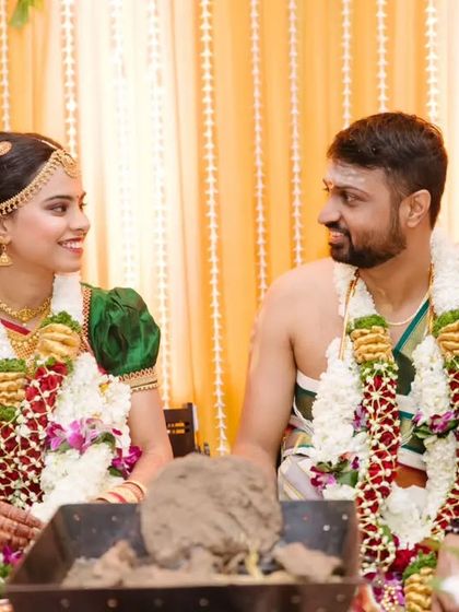 The couple shares a look of love while seated at their wedding ceremony, with the sacred fire in the foreground.