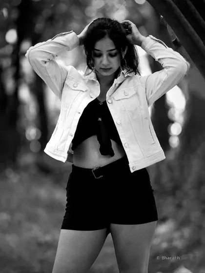 A candid-style monochrome portrait in a natural setting. The model is adjusting her hair, creating a spontaneous and authentic feel.