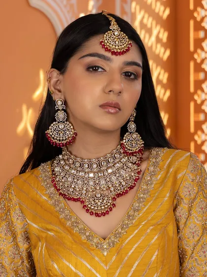 Our red Kundan bridal set is a perfect blend of traditional and contemporary craftsmanship. This full look, including the heavy choker, matching earrings, and maang tikka, is designed to give a bride a radiant glow on her wedding day.