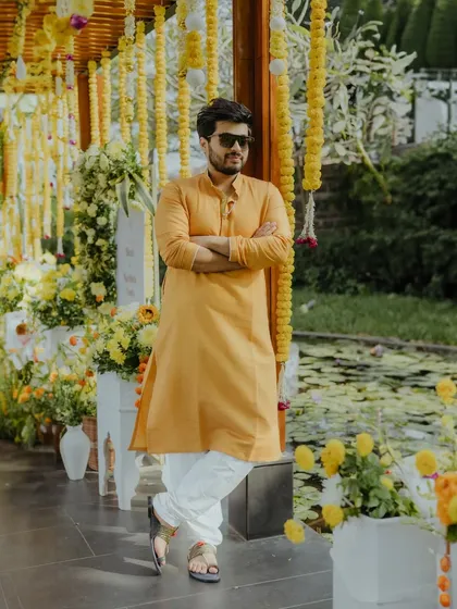 A stylish portrait of the groom in a mustard yellow kurta, posing against a backdrop of beautiful Haldi decor.