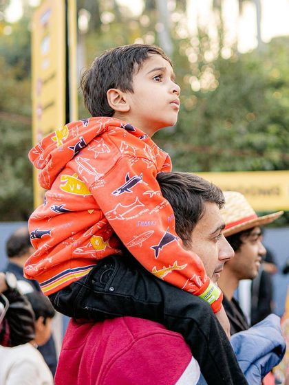 A young boy sits on his father's shoulders at Comic Con, looking up in awe. This candid shot captures the wonder and excitement of attending a big festival as a child.