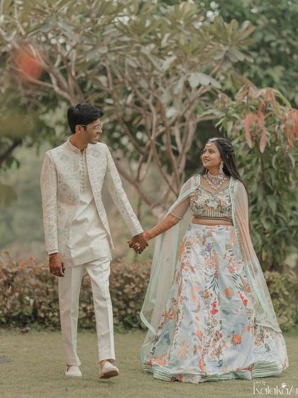 A classic portrait of the couple walking hand-in-hand through a lush garden. Their coordinated outfits look beautiful against the green backdrop.