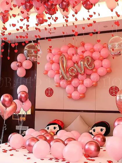 A sweet and charming room decoration featuring a large heart made of pink balloons with a "Love" sign. This setup is perfect for anniversaries or Valentine's Day, with cute character pillows adding a playful touch.