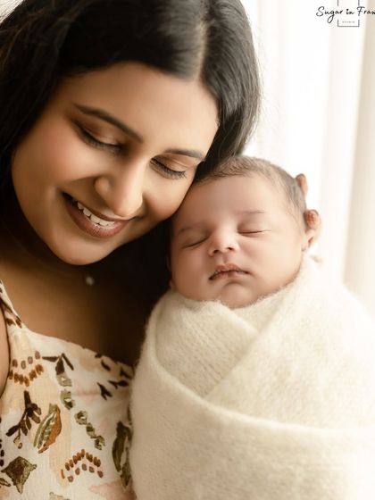 A close-up portrait of a new mother smiling as she holds her sleeping newborn. The soft lighting highlights the peaceful bond between them.