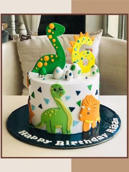 A delightful dinosaur-themed cake featuring friendly green and yellow dinos, eggs, and a big number six for a prehistoric party.