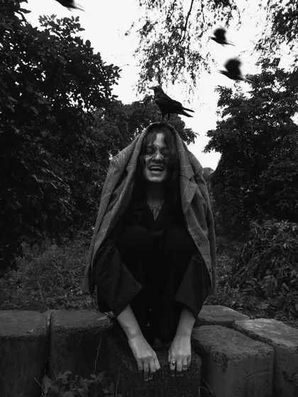 A surreal and slightly unsettling outdoor portrait. The birds surrounding the model, with one perched on her head, create a narrative that feels like a dark fairytale.