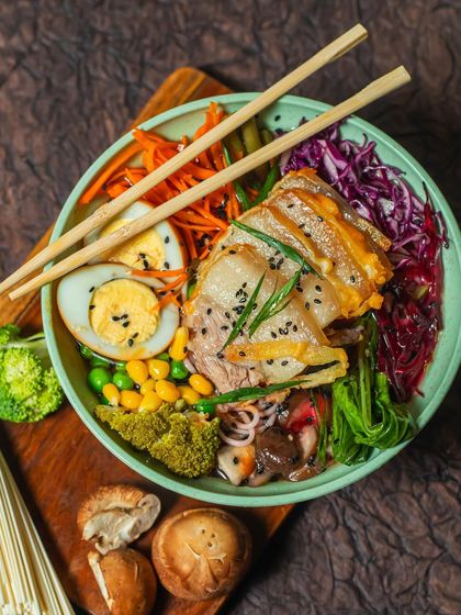 Our take on a classic Ramen bowl, loaded with flavour and texture. This bowl features tender noodles in a rich broth, topped with sliced pork, a soft-boiled egg, sweet corn, broccoli, and crisp carrots, all sprinkled with black sesame seeds.