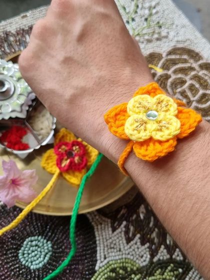A close-up of our floral crochet rakhi being worn. The vibrant orange and yellow flower stands out beautifully.