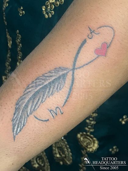 An infinity symbol created with a feather, with the initials 'A' and 'M' and a pink heart.